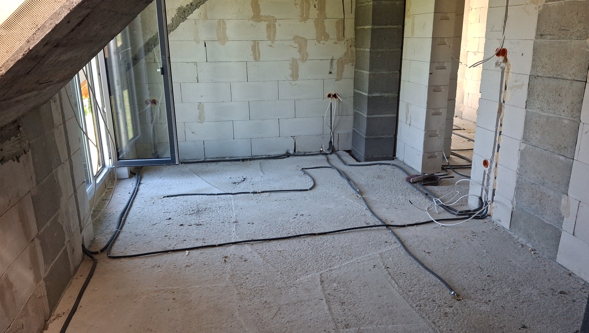 Surowy stan poddasza z widoczną instalacją elektryczną w bruzdach ścian i podłodze. Kable ułożone równolegle, przygotowane do zalania wylewką. Widoczne puszki elektryczne.