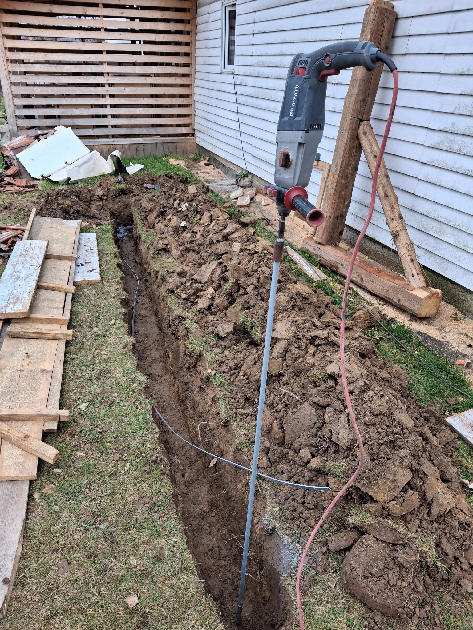 Wykop w ziemi z kablem, wbitym prętem i wiertarką udarową Graphite. Instalacja kabla w ziemi na zewnątrz budynku.