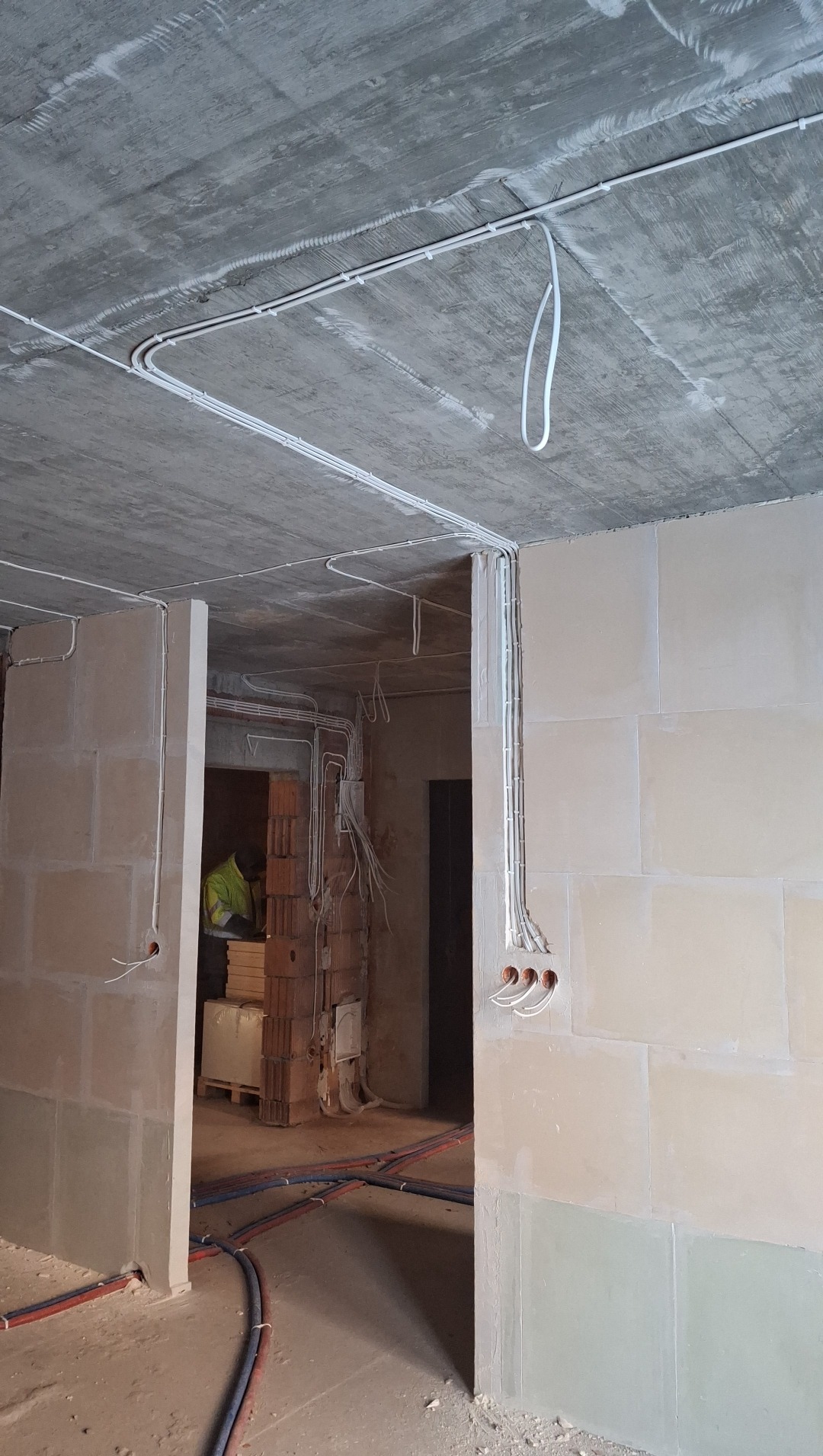 Surowy stan: białe kable elektryczne prowadzone po suficie i ścianach w nowym budynku, widoczne puszki instalacyjne.  Przewody pod podłogą.
