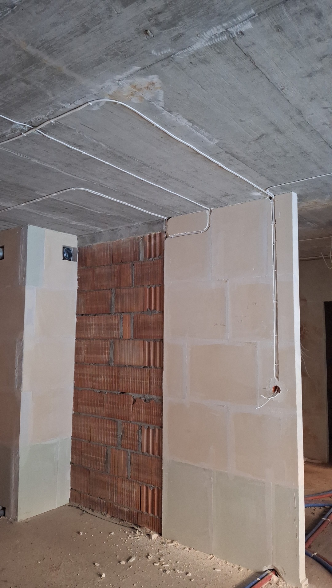 Białe kable elektryczne poprowadzone po suficie i ścianach w surowym wnętrzu. Widoczny fragment ściany z cegły i instalacje podtynkowe.