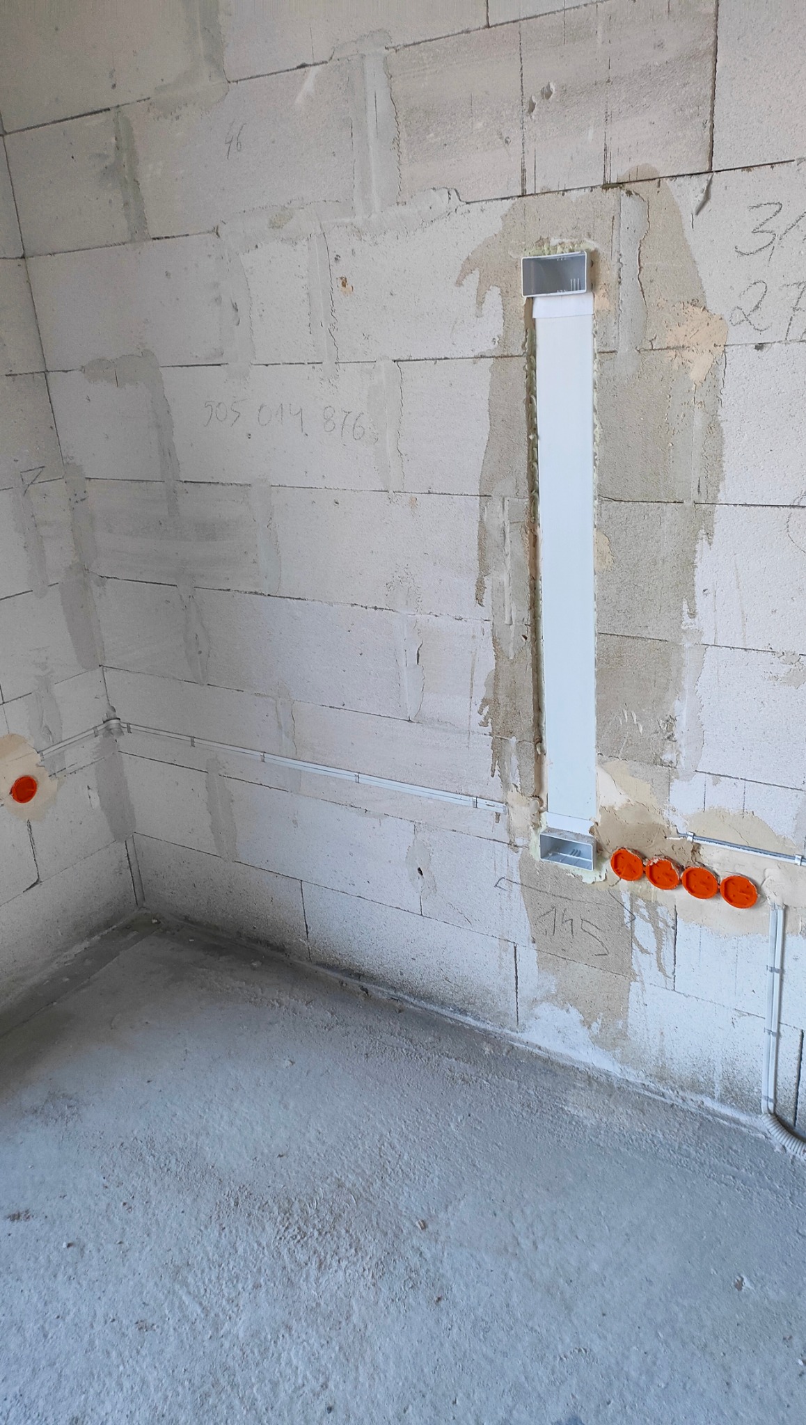 Surowy stan: ściany z betonu komórkowego z instalacją elektryczną w peszlach i puszkach. Pionowy kanał kablowy zamontowany na ścianie. Widoczne napisy na ścianie.