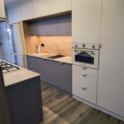 Markos usługi stolarskie Marcin Kołos - Nowoczesna kuchnia w odcieniach szarości i beżu, z drewnianym akcentem na ścianie i sprzętem AGD marki SMEG. Minimalistyczne fronty i drewniana podłoga.