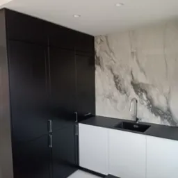 Nowoczesna kuchnia z czarnymi szafkami i białymi frontami, marmurowy backsplash, czarny blat i zlew. Minimalistyczny design z oświetleniem punktowym.