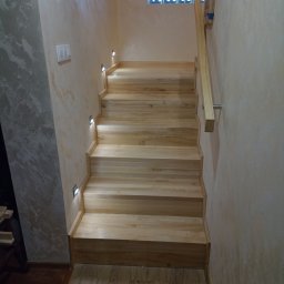 Markos usługi stolarskie Marcin Kołos - Jasne, drewniane schody z oświetleniem punktowym wzdłuż ściany, widok z dołu. Szklane luksfery w oknie u góry. Minimalistyczny styl, naturalne materiały i ciepłe światło.