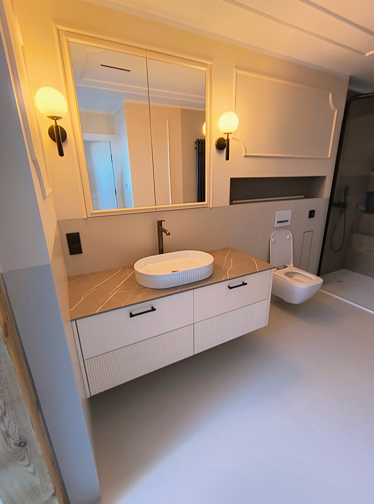 Elegancka łazienka z umywalką nablatową na szafce z ryflowanym frontem, lustrem w ramie i oświetleniem punktowym. Widoczna toaleta i kabina prysznicowa.