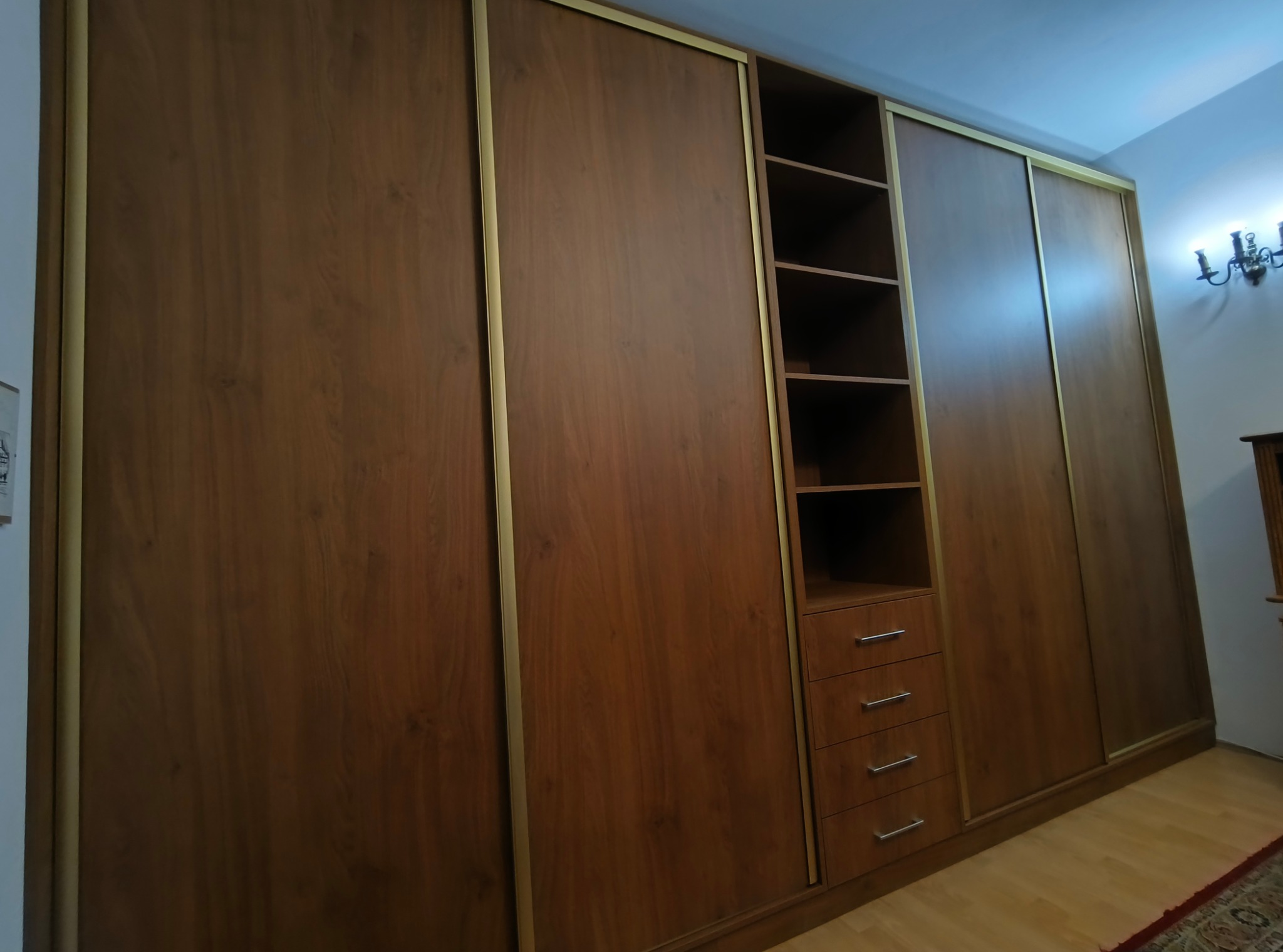 Wnętrze: zabudowa wnękowa z drewna z przesuwnymi drzwiami, półkami i szufladami. Uwagę zwracają złote obramowania frontów i delikatne oświetlenie.