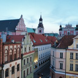 Kamil Cieslak - Panorama Starego Rynku w Poznaniu o zmierzchu. Widoczne kolorowe kamienice z czerwonymi dachami, wieże kościołów i ratusz w oddali.