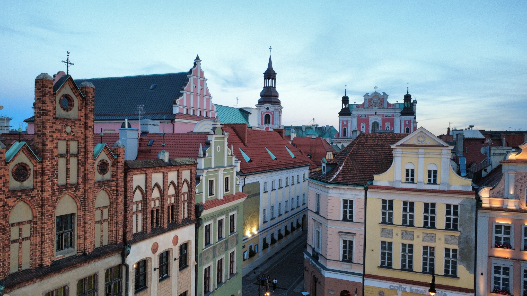 Panorama Starego Rynku w Poznaniu o zmierzchu. Widoczne kolorowe kamienice z czerwonymi dachami, wieże kościołów i ratusz w oddali.