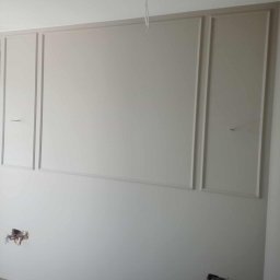 Rat-Bau Janusz Ratkiewicz - Ściana z dekoracyjnymi listwami w kolorze złamanej bieli, widoczne wystające kable instalacji elektrycznej. Element wykończenia wnętrza w trakcie prac.