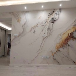 Artrewnetrza - Ściana z efektem marmuru w odcieniach bieli, złota i czerni, oświetlona punktowo, z widocznymi gniazdkami elektrycznymi i fragmentem podłogi z jasnych paneli.