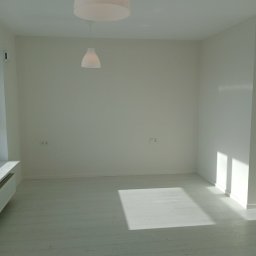 Artrewnetrza - Jasne, minimalistyczne wnętrze po remoncie: białe ściany, podłoga z desek, nowoczesne lampy wiszące. Wpadające promienie słoneczne podkreślają czystość i świeżość.