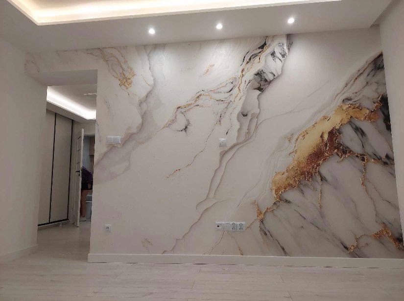 Ściana z efektem marmuru w odcieniach bieli, złota i czerni, oświetlona punktowo, z widocznymi gniazdkami elektrycznymi i fragmentem podłogi z jasnych paneli.