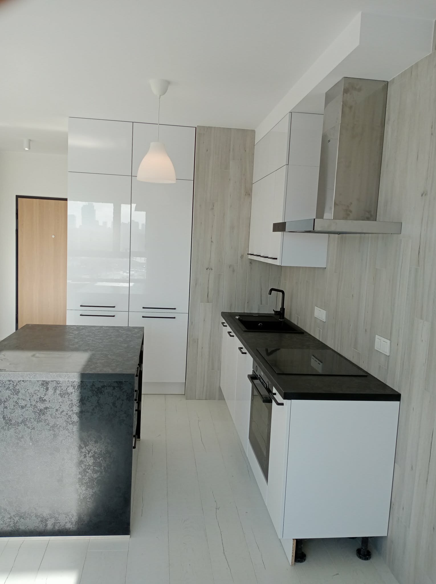 Nowoczesna kuchnia z wyspą: białe szafki, czarny blat, drewnopodobne panele ścienne i podłoga. Minimalistyczny design, oświetlenie punktowe.