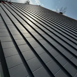 Nowoczesny dach z czarnej dachówki ceramicznej w kwadratowym formacie, lśniący w słońcu. Widok z dołu, podkreślający regularność wzoru i estetykę wykończenia.