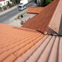 Mirosław Marciniak - Czerwona dachówka ceramiczna na ukończonym dachu domu, widok z góry, fragment ulicy i pracownik w tle. Dach po renowacji, wyraźna faktura dachówki.