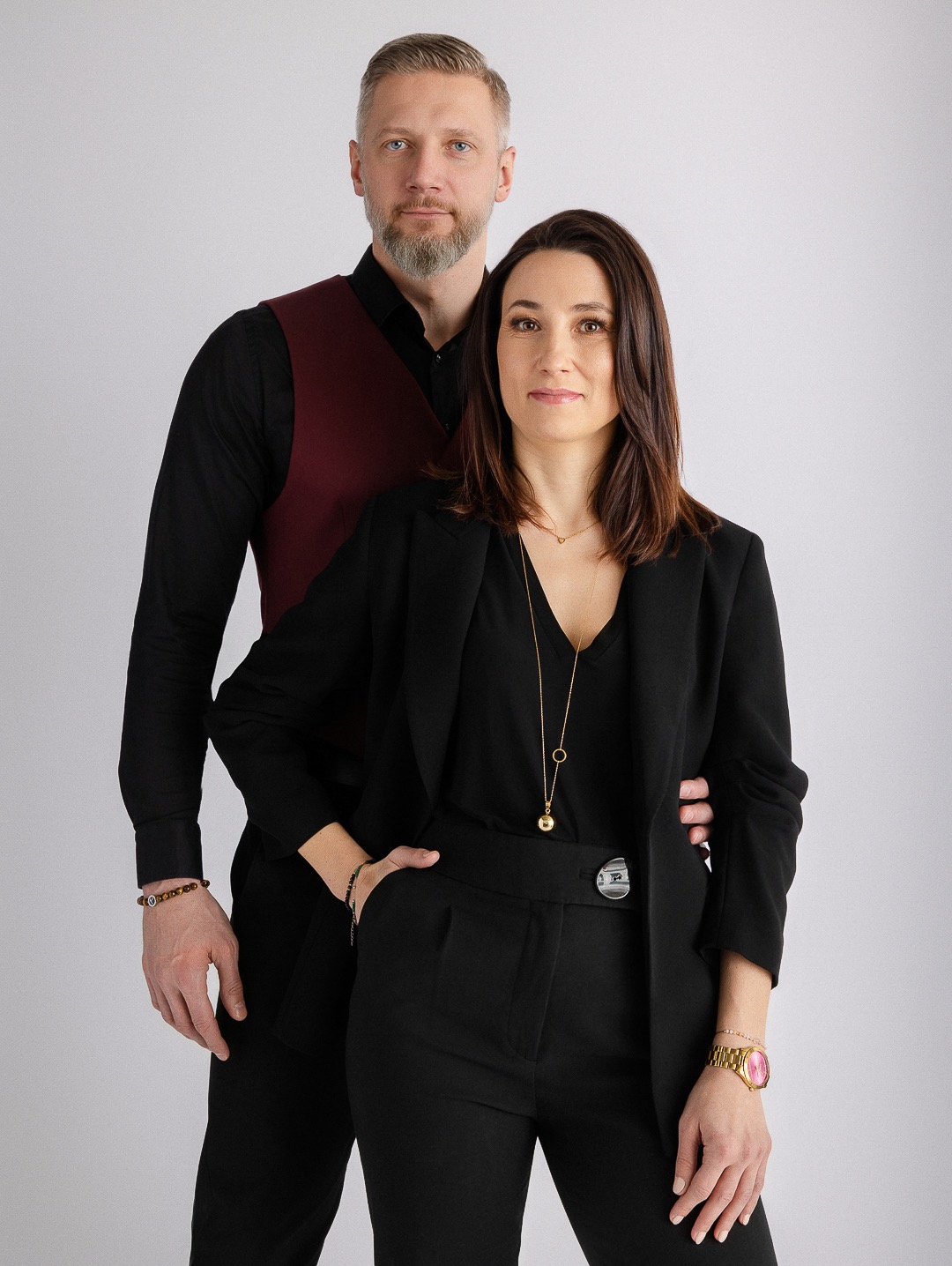Portret biznesowy kobiety w czarnym garniturze i mężczyzny w bordowej kamizelce na jasnym tle. Profesjonalna sesja wizerunkowa.