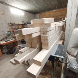 BERWOOD Jarosław Chwasta - Przygotowane elementy drewniane z nawierconymi otworami, ułożone na stole w warsztacie stolarskim. Widoczne narzędzia i surowy wystrój wnętrza.