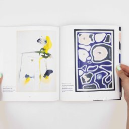 Ewa Pietruszko - Otwarta książka z abstrakcyjnymi obrazami w kolorach żółtym, niebieskim i fioletowym, trzymana przez dłonie z zielonym manicure na białym tle.