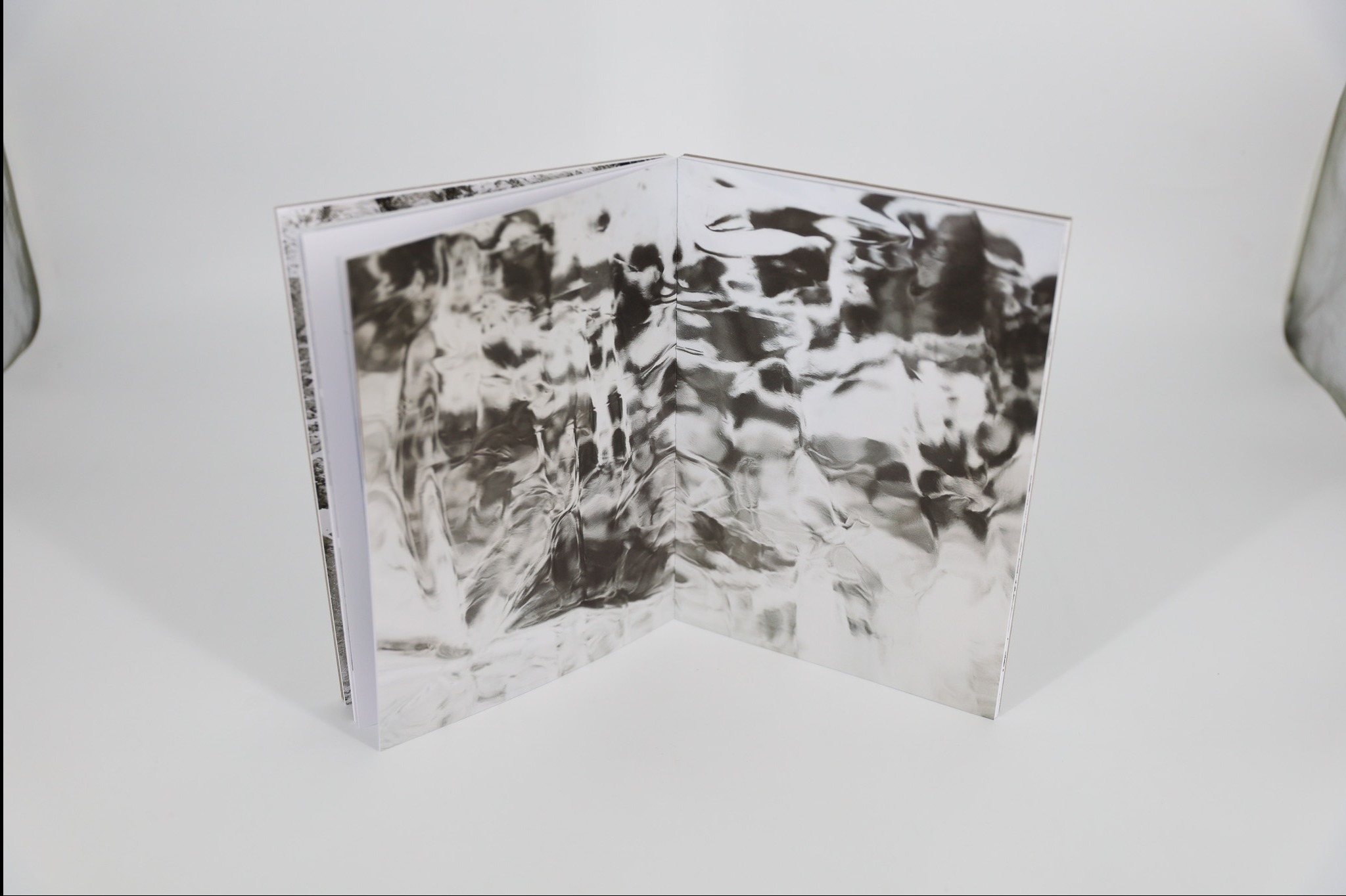 Otwarta książka z abstrakcyjnym, srebrzystym wzorem na okładce i stronach, leżąca na białym tle. Widoczne kartki i grzbiet książki. Minimalistyczna kompozycja.