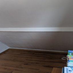 NOWY WYMIAR- Studio Projektów Justyna Matulewicz - Poddasze po remoncie: świeżo pomalowane ściany w odcieniach bieli i szarości, drewniana podłoga. Stos książek w rogu dodaje wnętrzu przytulnego charakteru.