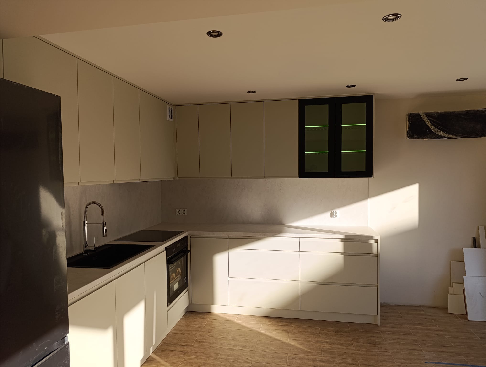 Jasna kuchnia z minimalistycznymi frontami szafek i czarnymi akcentami. Nowoczesny design z drewnopodobną podłogą i świeżym oświetleniem punktowym.