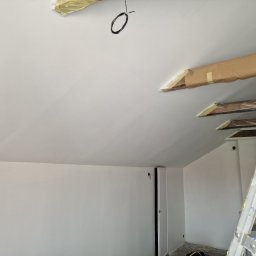 Gabriel Kłosiński - Białe ściany i sufit po malowaniu w poddaszu ze skosami. Widoczne zabezpieczone elementy drewniane i drabina malarska.