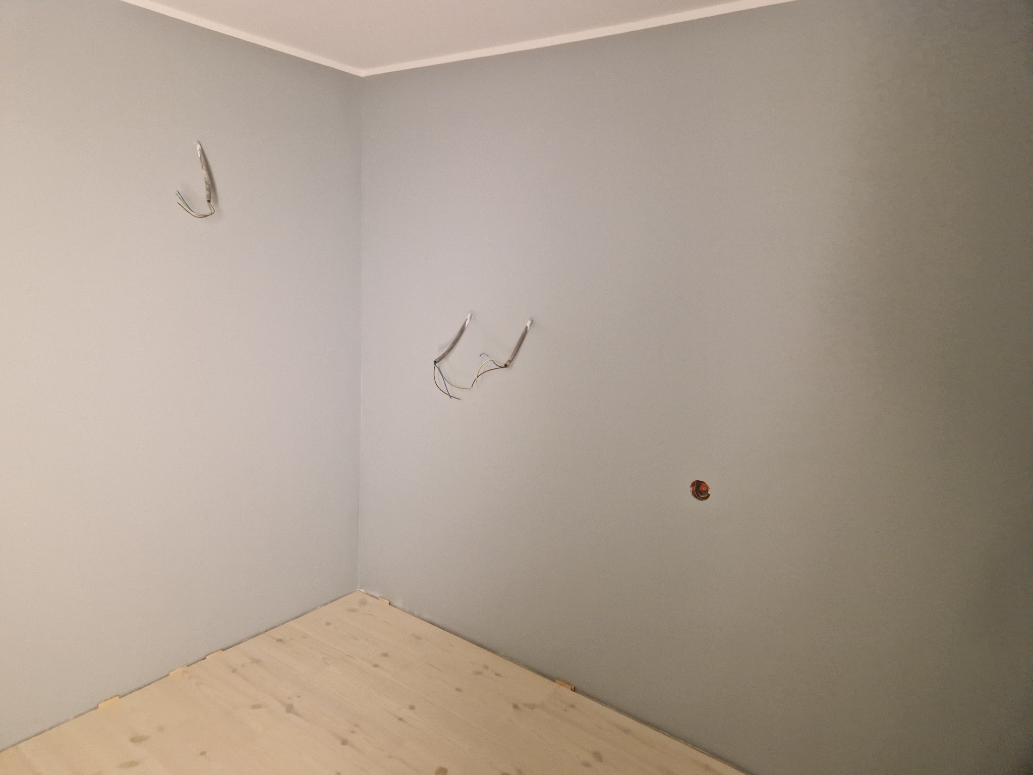Pokój w trakcie wykończenia w Szczecinie. Ściany pomalowane na szaro, widoczne kable elektryczne i fragment podłogi z jasnego drewna.