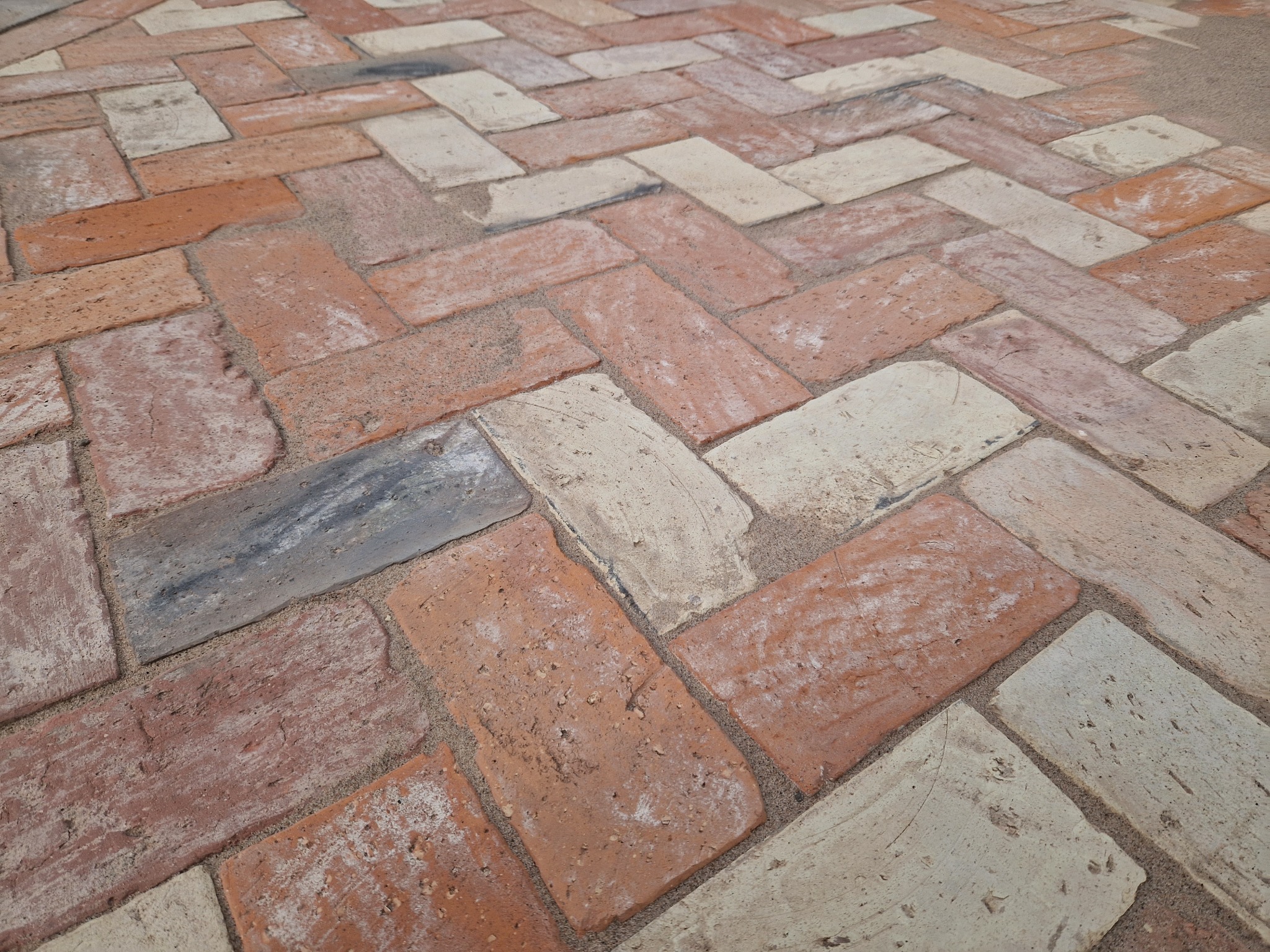 Ułożona kostka brukowa w jodełkę z ceglastych i beżowych elementów, widok z góry, fuga wypełniona piaskiem. Detal wykończonej nawierzchni.