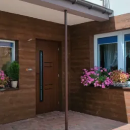 Elewacja domu z fakturą drewna, okna z kwiatami w doniczkach, brązowe drzwi z przeszkleniem. Eleganckie wykończenie zewnętrzne budynku.