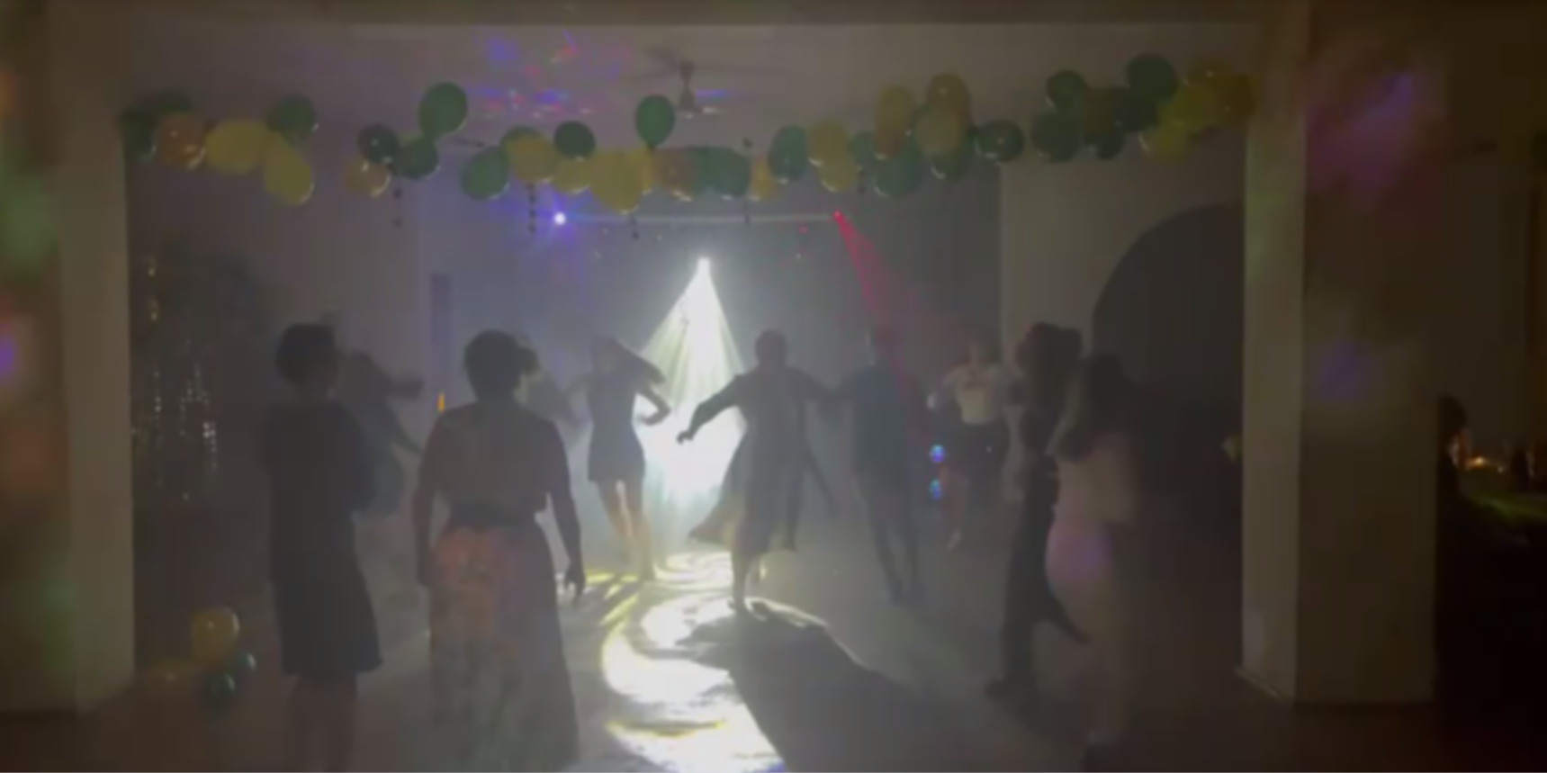 Rozświetlona sala balowa z tańczącymi osobami, dekorowana zielono-żółtymi balonami i efektami świetlnymi, tworząca dynamiczną atmosferę imprezy.