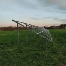 Metalowa konstrukcja wsporcza na łące, prawdopodobnie pod panele fotowoltaiczne. Widoczne elementy montażowe i naturalne otoczenie.