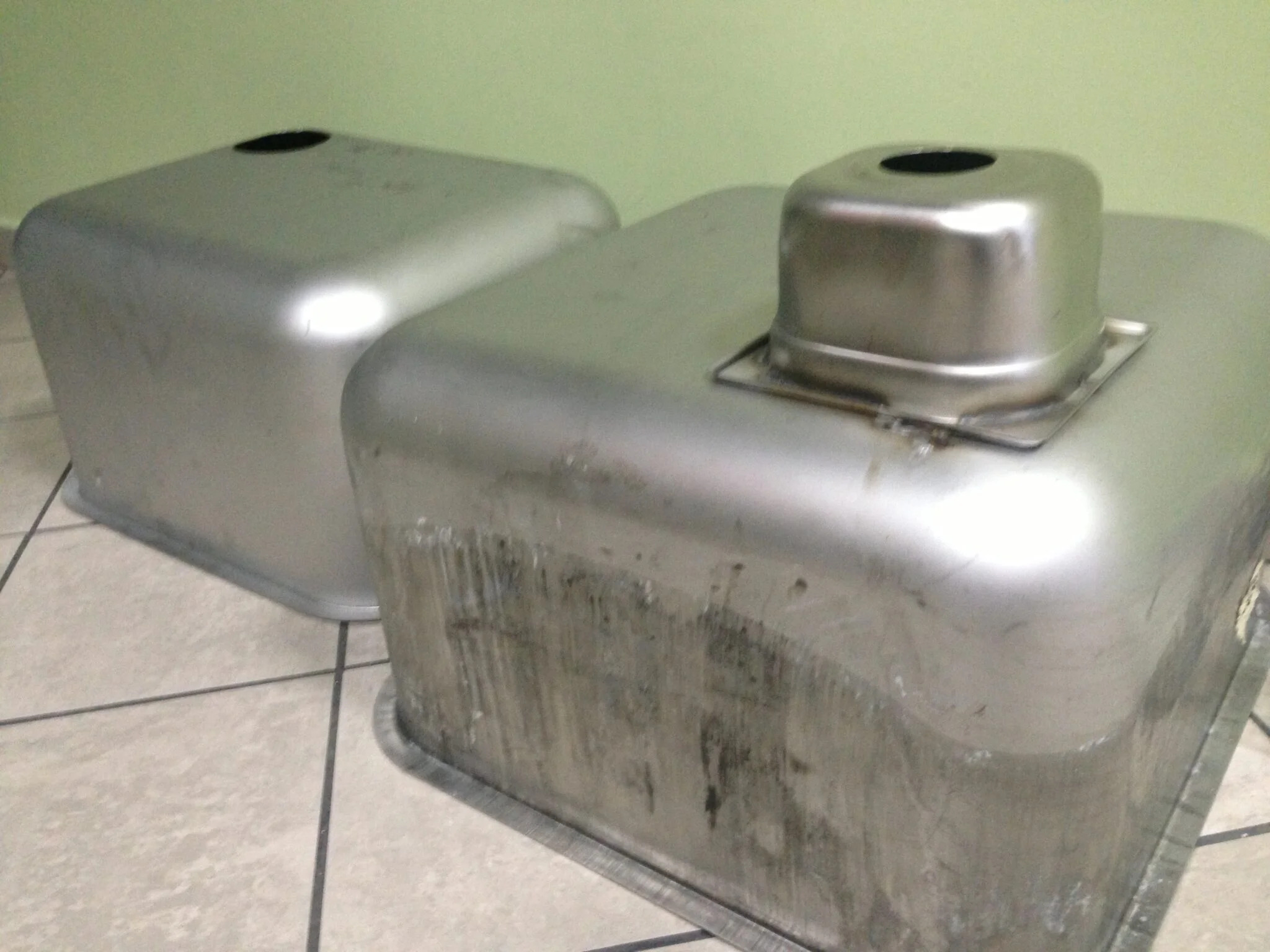 Dwie metalowe formy, jedna z otworem i mocowaniem, druga gładka, leżą na kafelkach. Widoczne ślady obróbki na boku formy z mocowaniem.