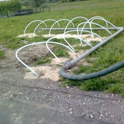 SKYWEATHER SPÓŁKA Z OGRANICZONĄ ODPOWIEDZIALNOŚCIĄ - Instalacja nawadniająca na trawiastym terenie, z widocznymi rurami i zraszaczami, podłączona do węża doprowadzającego wodę. System w trakcie rozkładania na gruncie.
