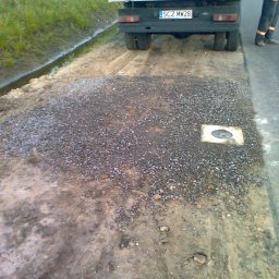 SKYWEATHER SPÓŁKA Z OGRANICZONĄ ODPOWIEDZIALNOŚCIĄ - Przygotowanie podłoża pod instalację, widoczny właz kanalizacyjny i ciężarówka z tablicą SCZ MW28. Grunt częściowo pokryty żwirem.