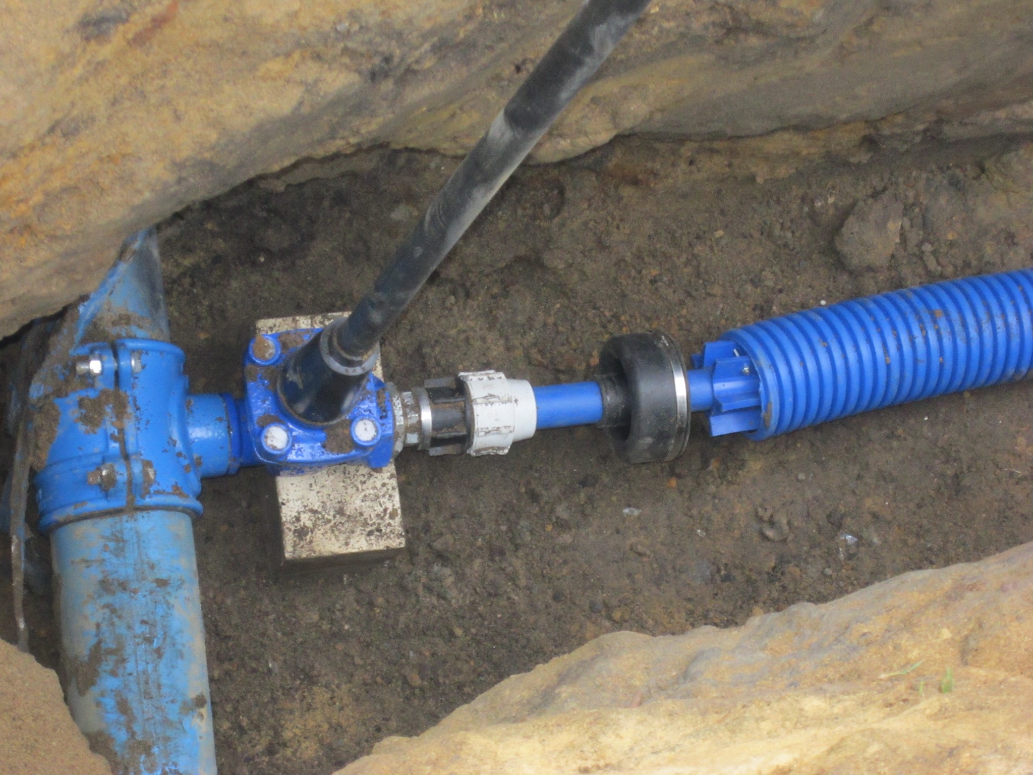 Niebieskie rury kanalizacyjne połączone z kablem w wykopie ziemnym, widoczne złącza i elementy instalacji.