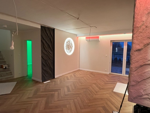 Salon po wykończeniu: parkiet w jodełkę, dekoracyjny panel ścienny, okrągła lampa, klimatyzacja i kolumna z imitacji kamienia. Nowoczesne oświetlenie.