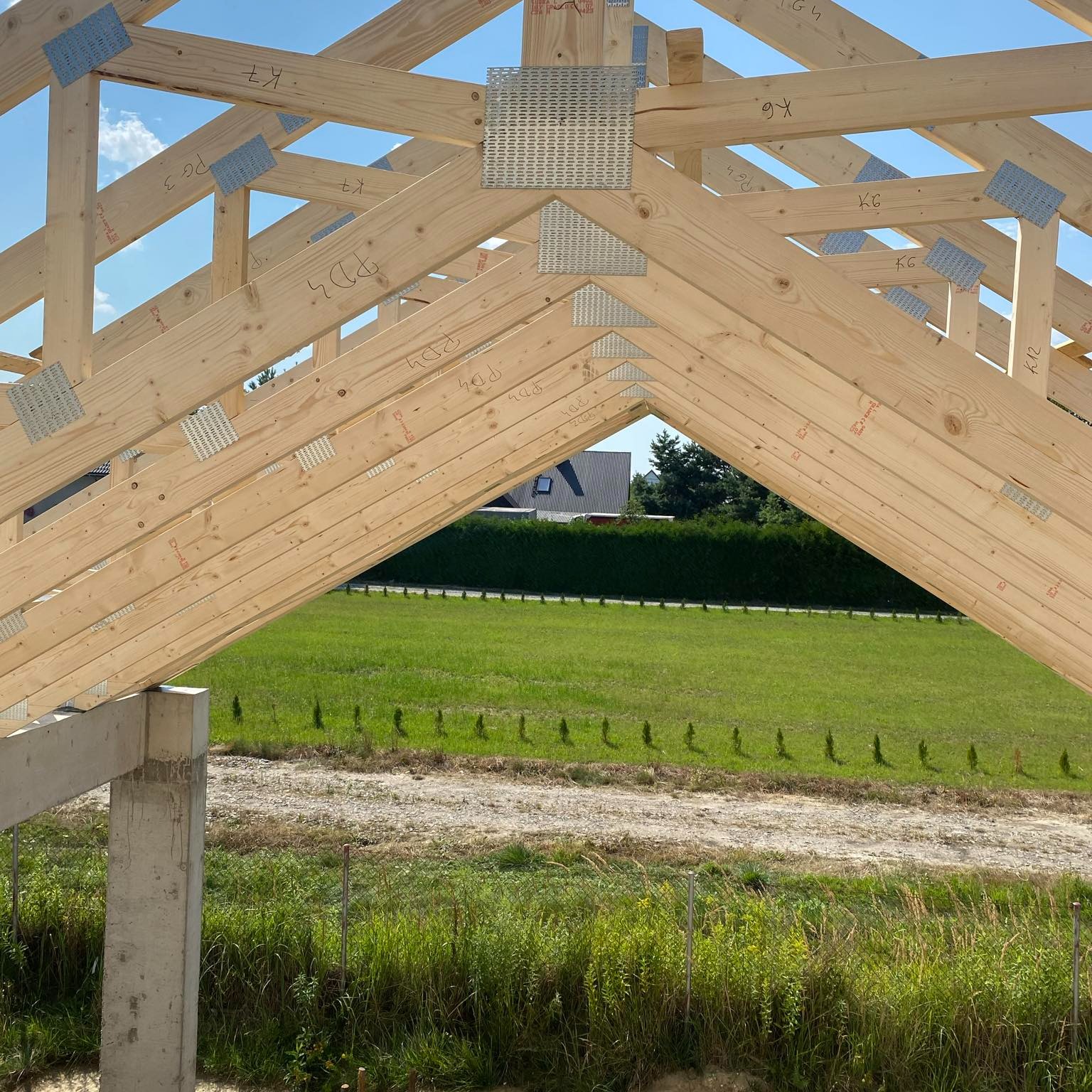 Konstrukcja drewniana dachu z widocznymi złączami metalowymi, na tle zielonego krajobrazu w Lublinie. Elementy więźby dachowej z bliska, w trakcie montażu.