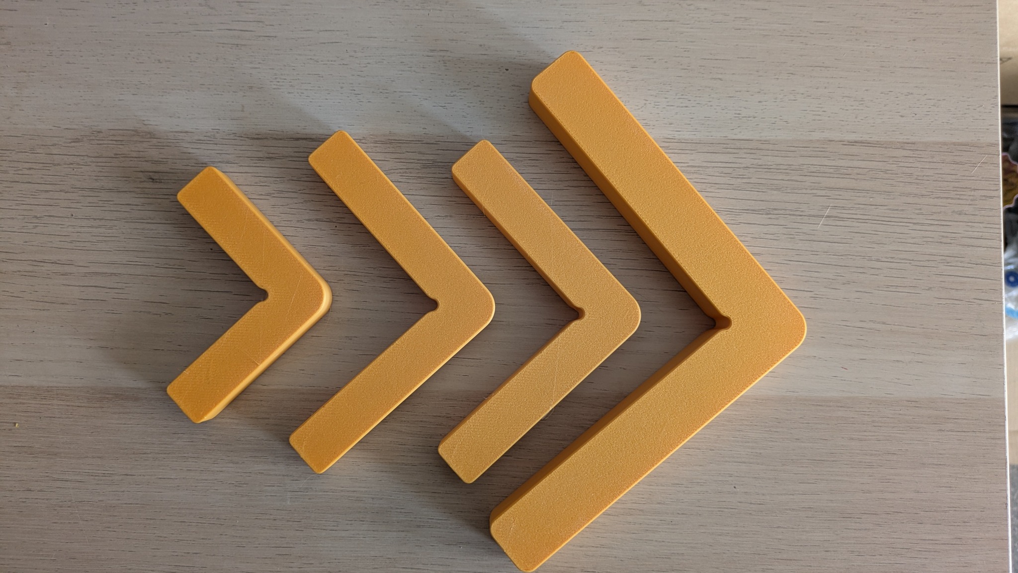 Żółte elementy w kształcie strzałek, wydrukowane w 3D, ułożone w rzędzie od najmniejszego do największego, na drewnianym blacie.