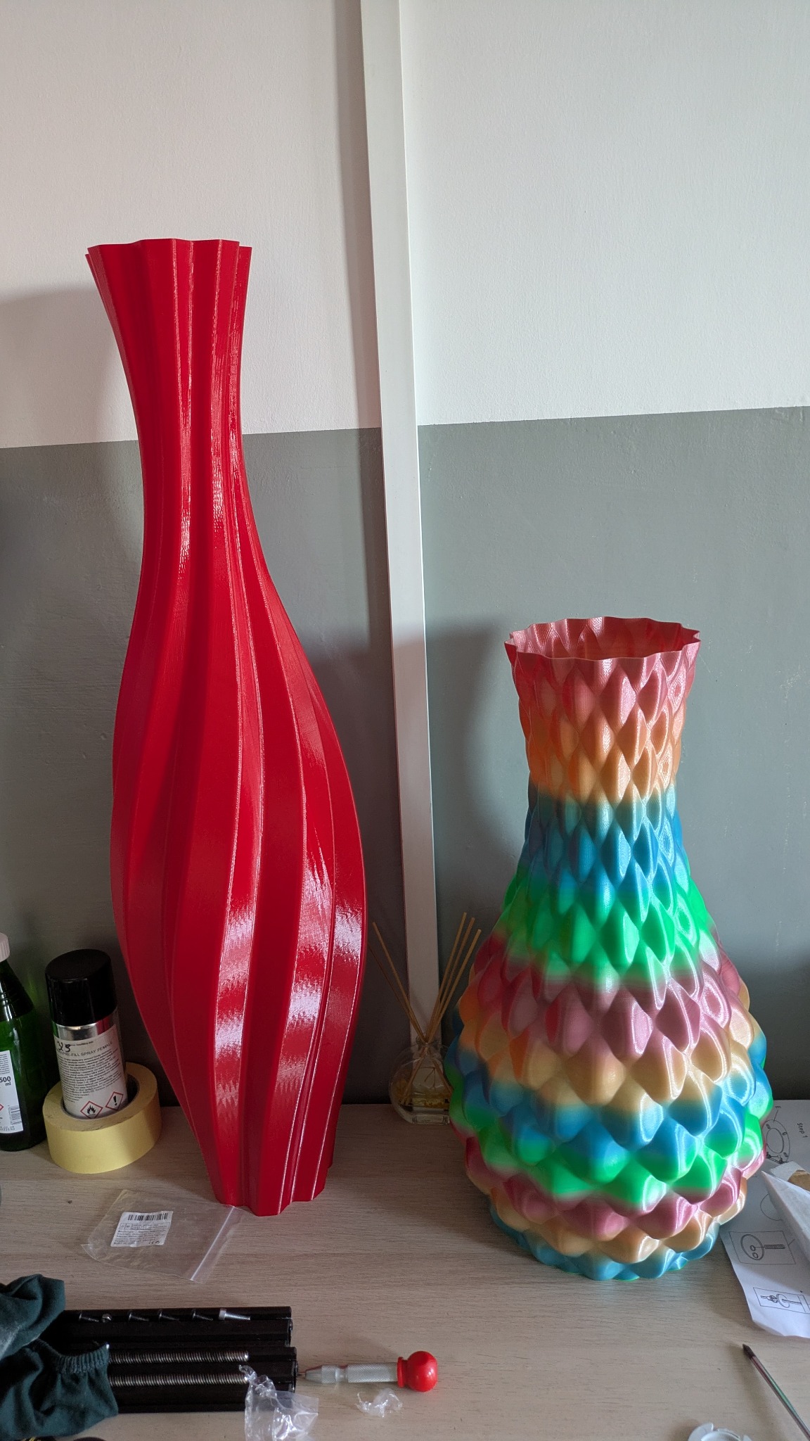 Dwie wazy: wysoka, czerwona o spiralnym wzorze i krępa, wielobarwna o fakturze przypominającej łuski, wykonane prawdopodobnie metodą druku 3D.