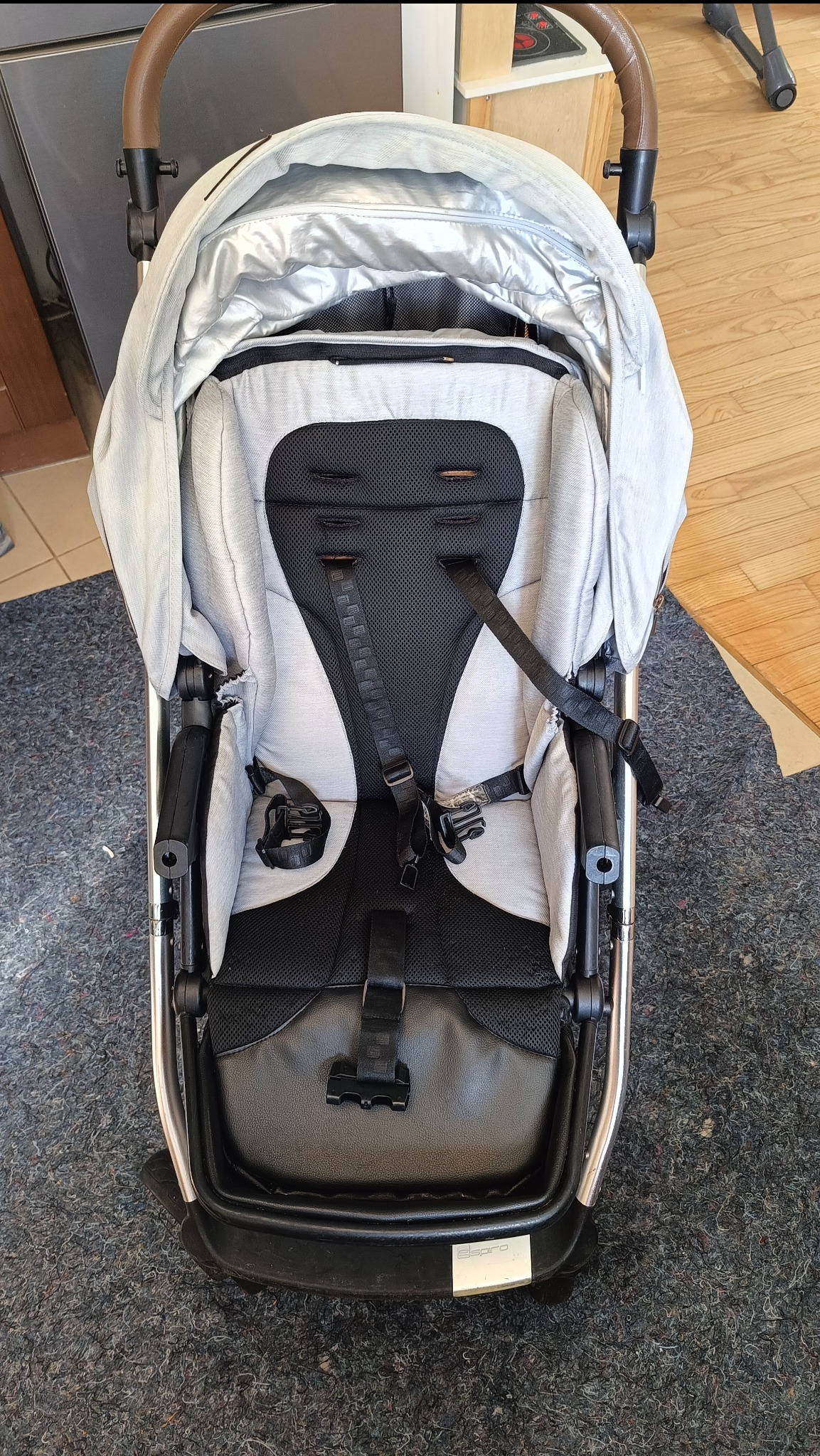 Wózek dziecięcy Espiro z szarą tapicerką i czarnymi elementami, widoczny z góry na tle szarego dywanu.