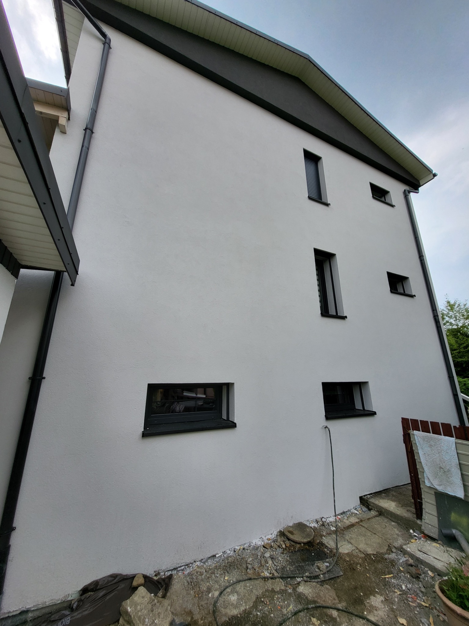 Biała elewacja domu z czarnymi oknami i orynnowaniem w Krakowie. Widok z dołu, podkreślający nowoczesny wygląd budynku.