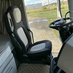 Ekipa czystości - Wnętrze kabiny ciężarówki: czarno-szare fotele z wzorem, kierownica i widok na zewnątrz przez szybę. Uwagę zwraca czystość i dbałość o detale wykończenia.