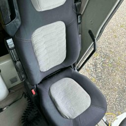 Ekipa czystości - Wnętrze kabiny pojazdu z ciemnoszarym fotelem z jasnoszarą tapicerką, widoczny pas bezpieczeństwa i elementy sterowania. Fotel czysty i zadbany.