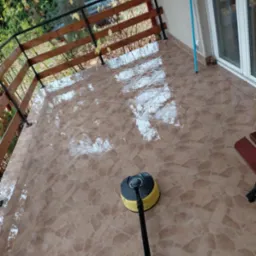 Czyszczenie terakoty na balkonie za pomocą szorowarki Karcher. Widoczne mokre płytki i balustrada. Praca w toku, zieleń w tle.