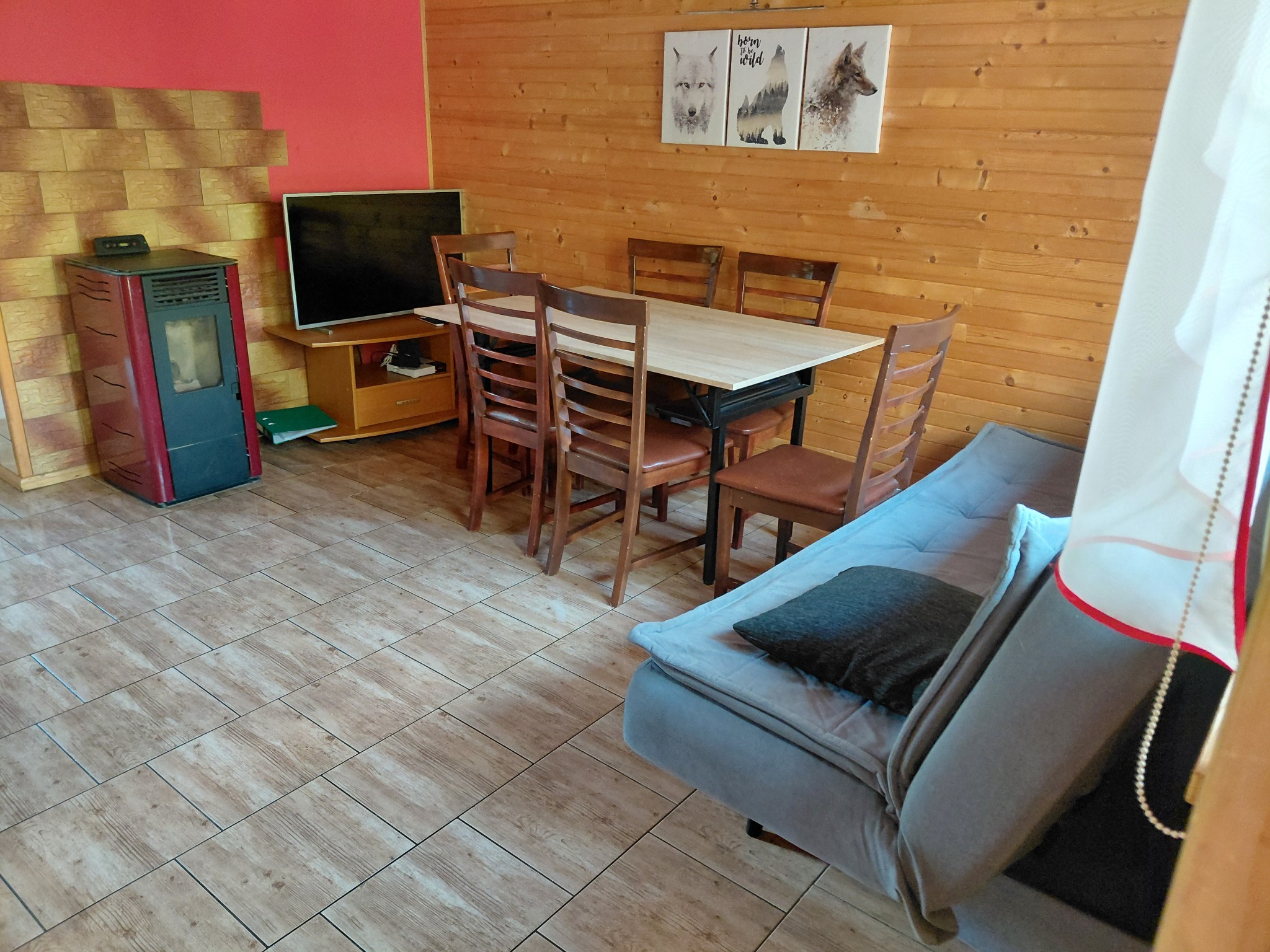 Salon po sprzątaniu w Sanoku: drewniane ściany, stół z krzesłami, sofa z poduszką, piec, telewizor i podłoga z płytek imitujących drewno. Utrzymany porządek i czystość.