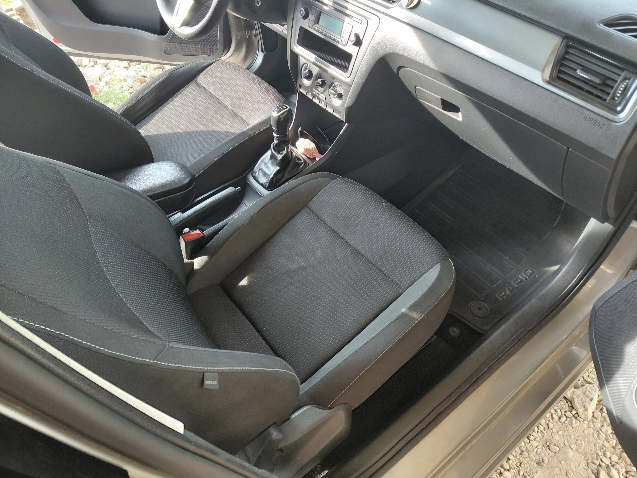 Wnętrze samochodu z czarną tapicerką, widoczne przednie fotele, deska rozdzielcza i dywaniki z logo 'RAPID'. Czyste i zadbane wnętrze pojazdu.