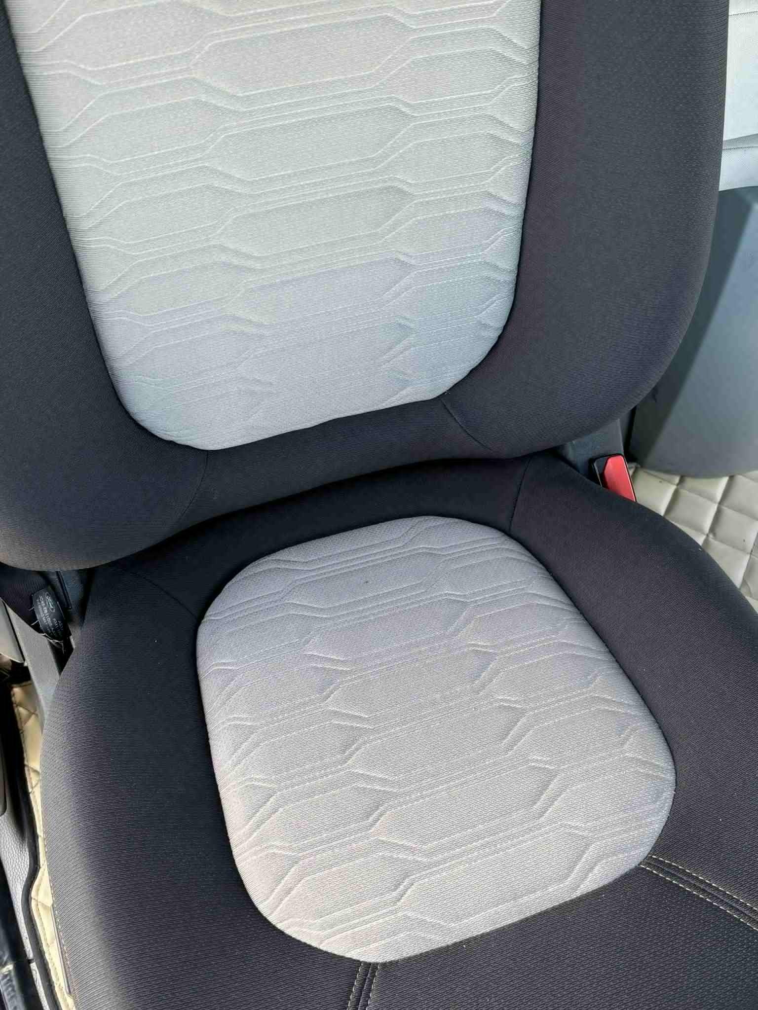 Szczegółowe ujęcie wyczyszczonego, jasnego fotela samochodowego z ciemną obwódką. Widoczna faktura materiału i szwy. Czysty i zadbany wygląd.