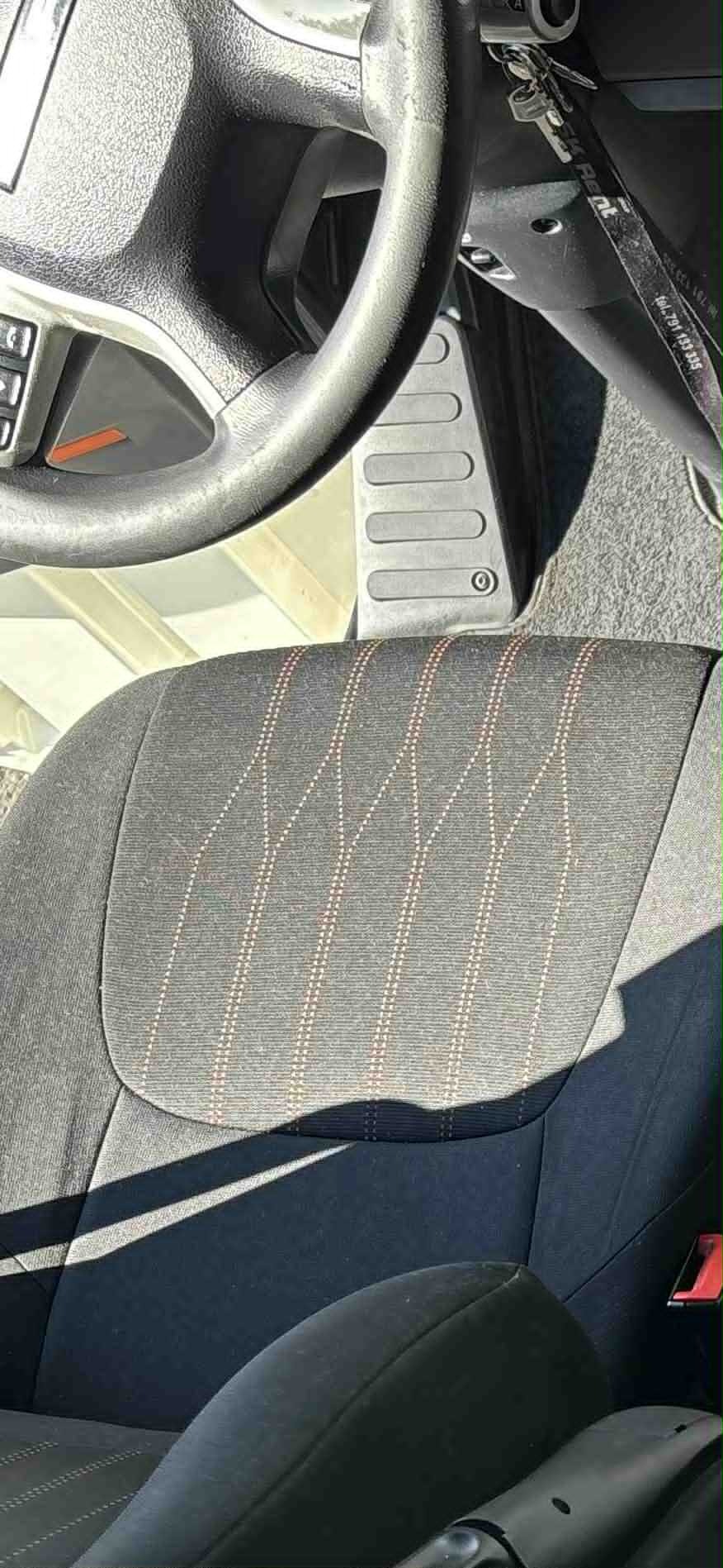 Wnętrze auta z widocznym fotelem z szarą tapicerką w prążki, kierownicą i fragmentem deski rozdzielczej. Na kierownicy zawieszone klucze z brelokiem.