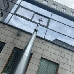 Mycie okien na wysokości budynku biurowego za pomocą teleskopowej lancy ze szczotką. Widoczny fragment elewacji z oknami i odbicie nieba w szybach.