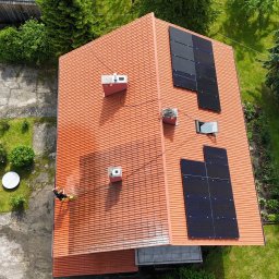 AlpinPeak - Z góry: Czyszczenie dachu z dachówki ceramicznej z panelami słonecznymi. Widoczny pracownik w trakcie pracy, strumień wody i różnica w czystości powierzchni.